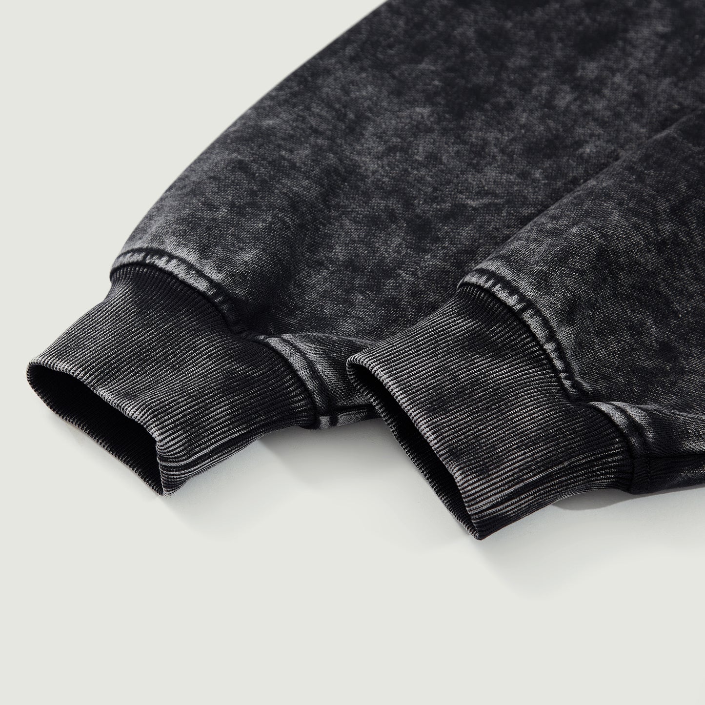 Detail shot of black snow-wash hoodie cuff showing thick cotton fabric and ribbed finish.