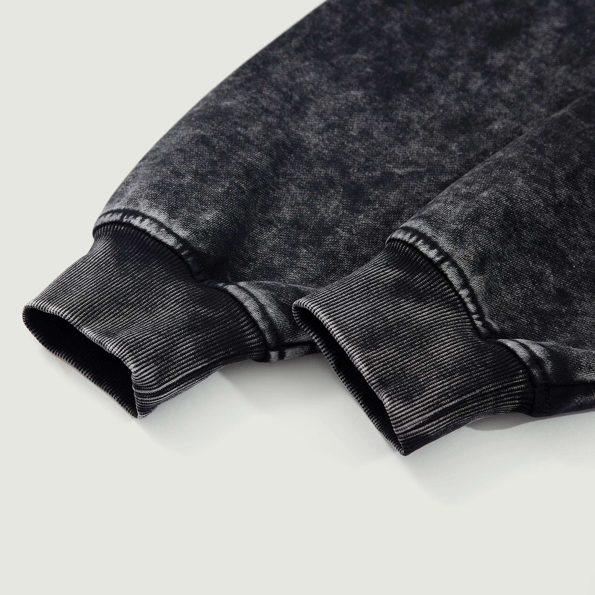 Detail shot of black snow-wash hoodie cuff showing thick cotton fabric and ribbed finish.