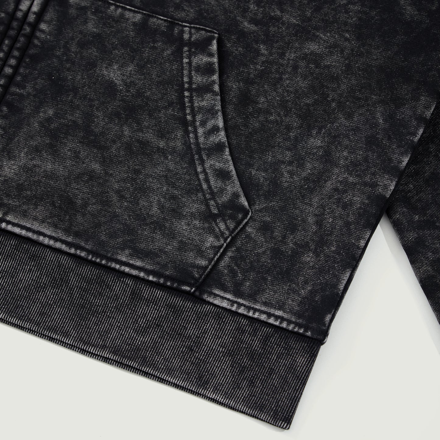 Detail shot of black snow-wash hoodie hem showing washed fade pattern and stitching.