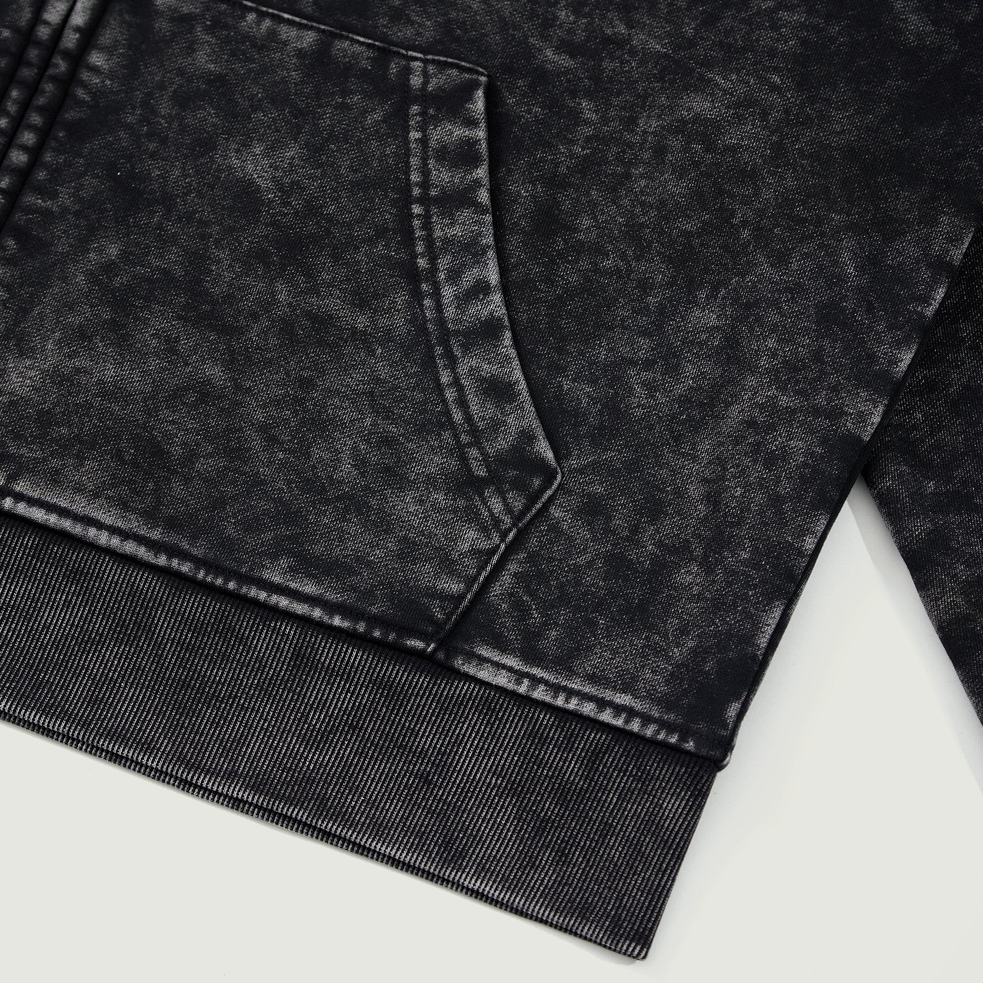 Detail shot of black snow-wash hoodie hem showing washed fade pattern and stitching.