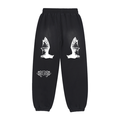 Washed black unisex sweatpants feature two white bat wing graphics and the text "GRAVE DANCER" on the back. They have an elasticated waistband with drawstrings and elasticated cuffs.
