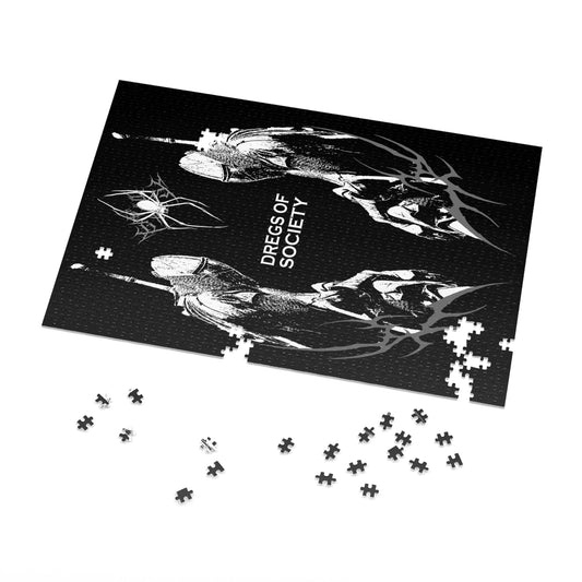 A 1000-piece jigsaw puzzle with a glossy finish displays a black background with a white graphic of two figures in gas masks flanking the text "DREGS OF SOCIETY" and a spider-like design. Some loose puzzle pieces are scattered around the assembled portion. The puzzle comes in a white metal tin with the same image on the lid.