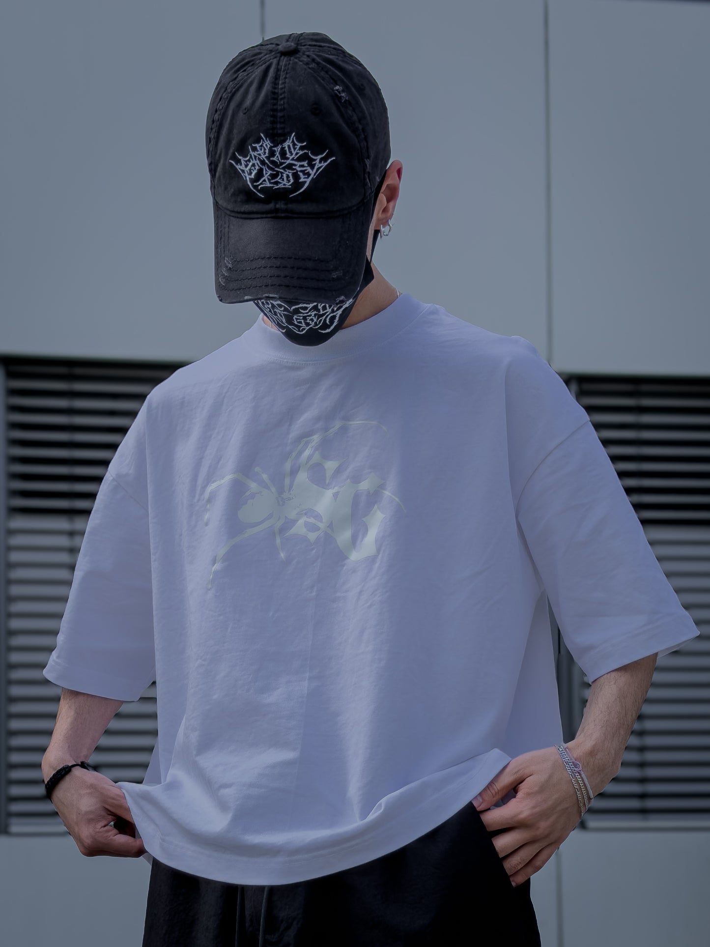 Person wearing a white t-shirt with a graphic design and a black cap, standing against a plain background.