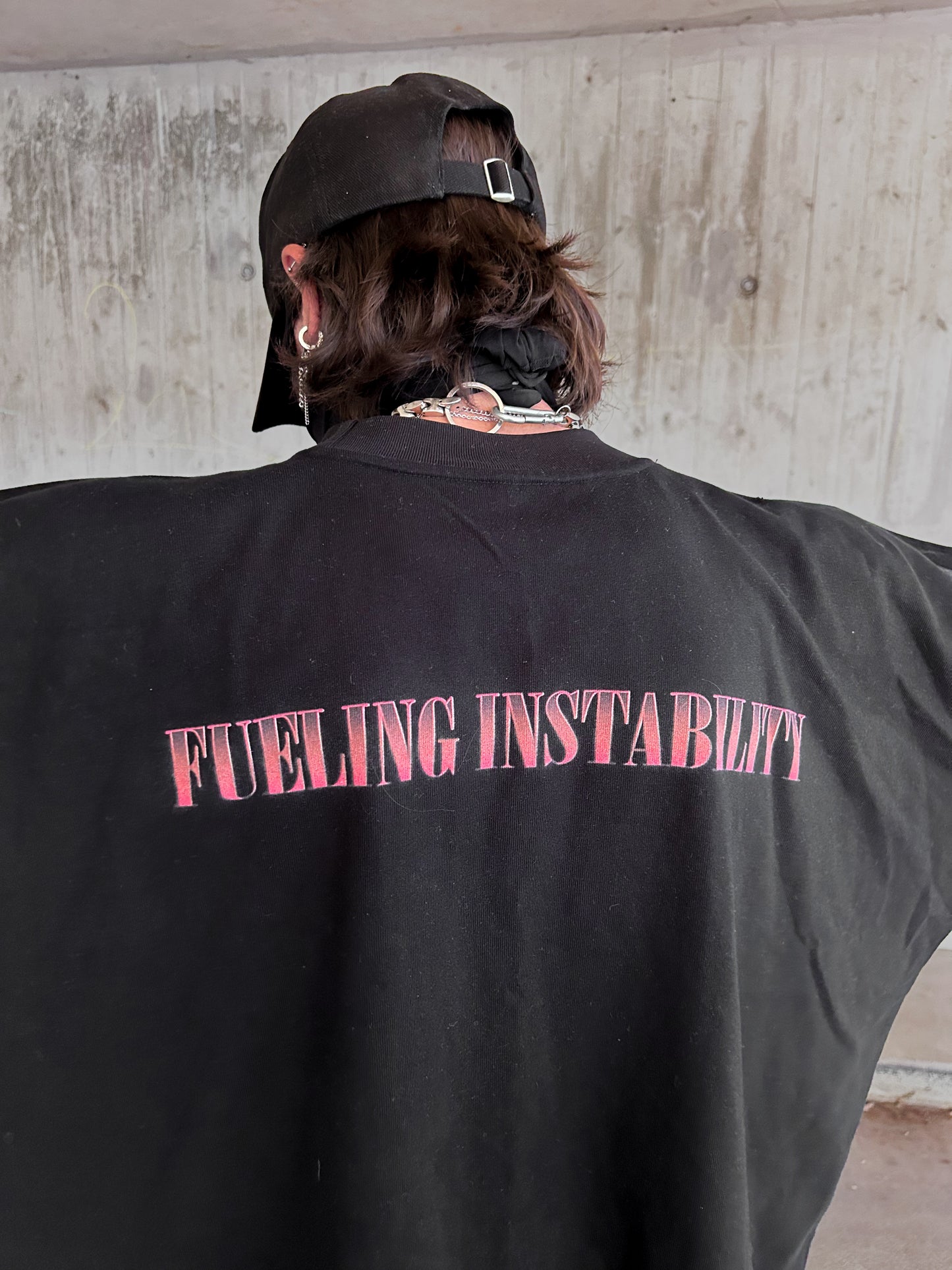 Back view of a person wearing a black shirt with ‘FUELING INSTABILITY’ printed in red.