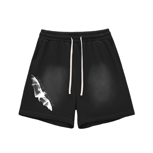 Washed black unisex shorts feature a white graphic of a bat wing and the text "GRAVE DANCER" on the left leg. They have an elasticated waistband with white drawstrings and side pockets.