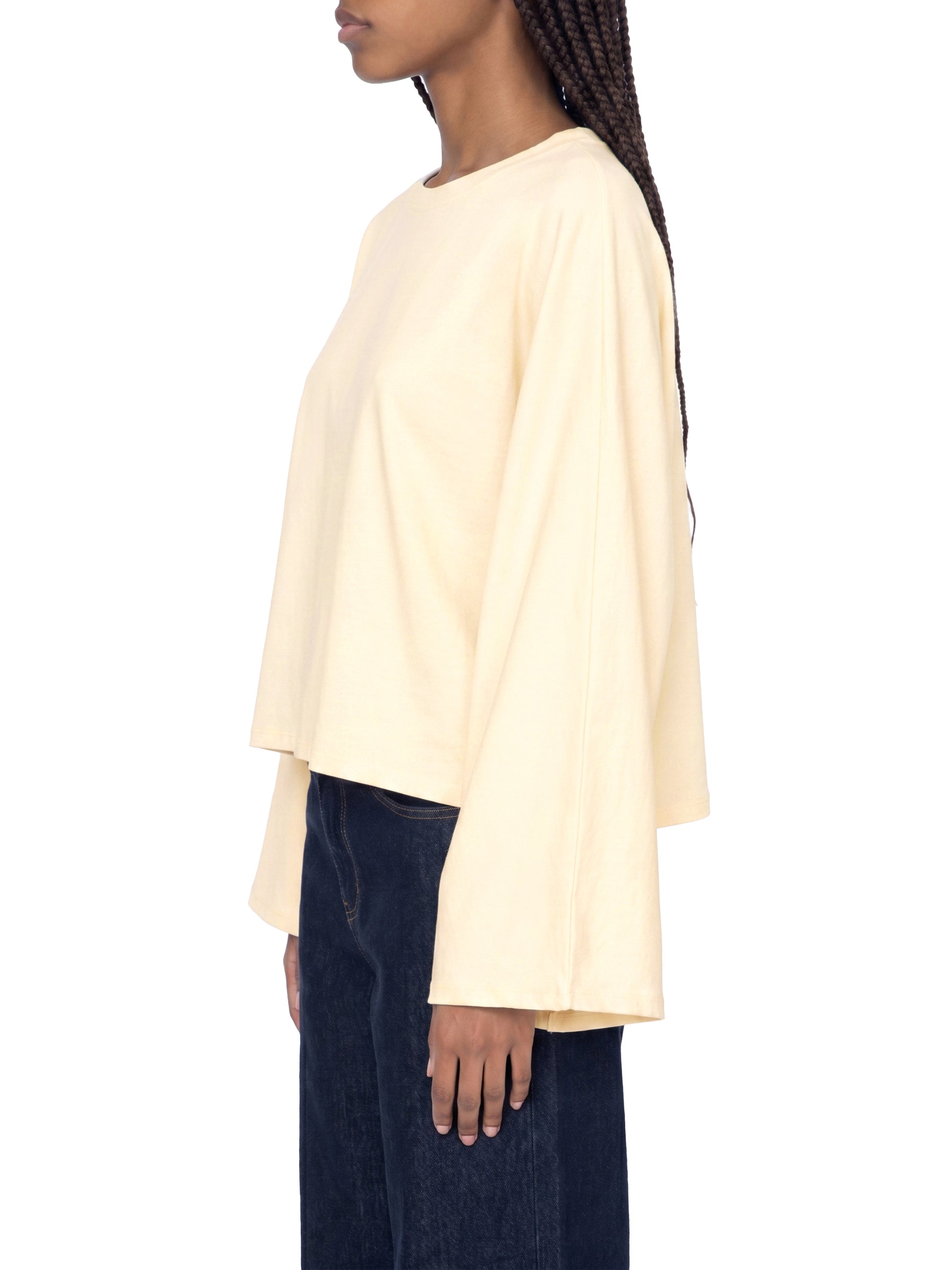 Person wearing a light yellow long-sleeve top and dark jeans on a white background