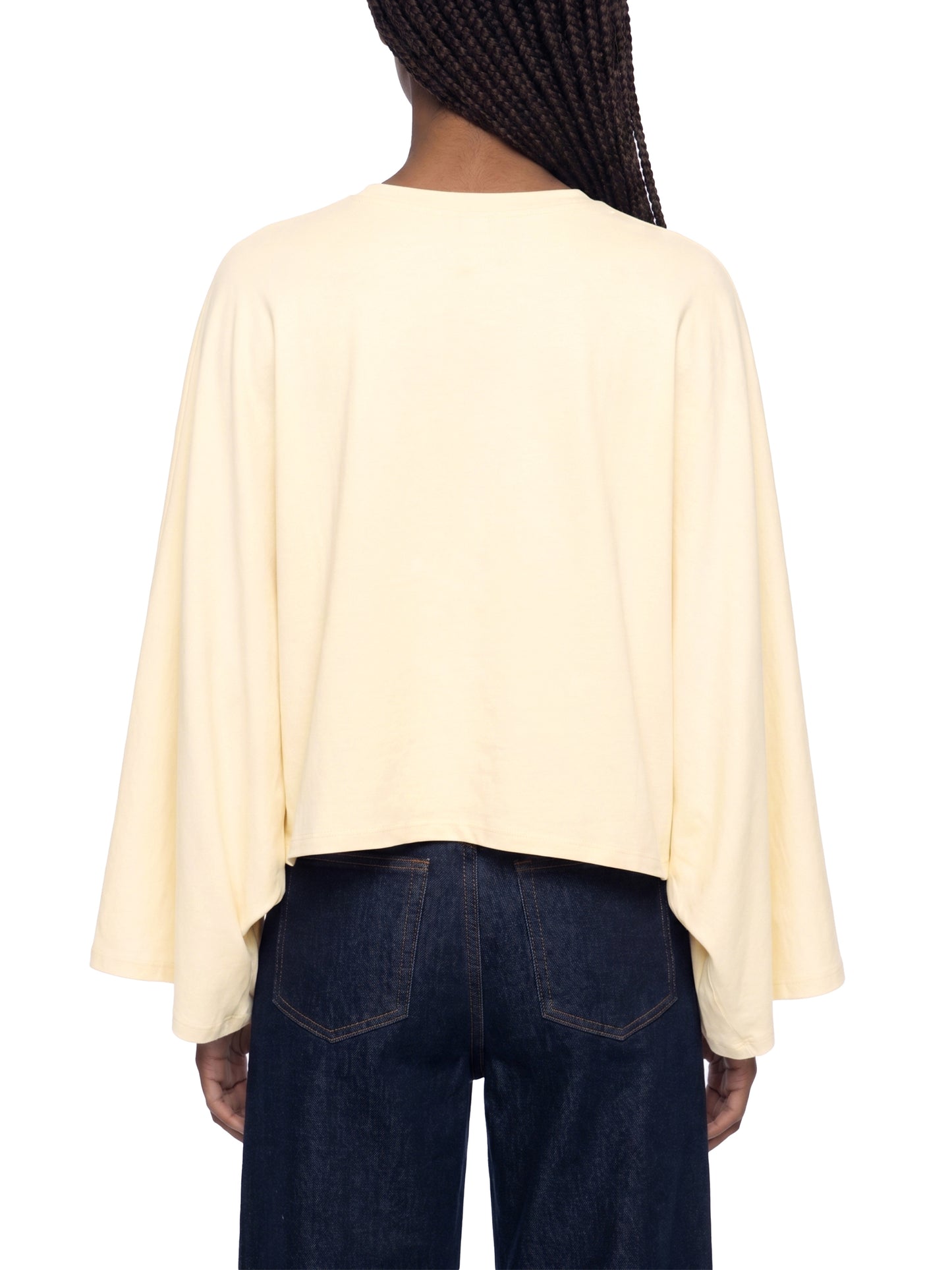 Person wearing a light yellow cape over dark blue jeans on a white background