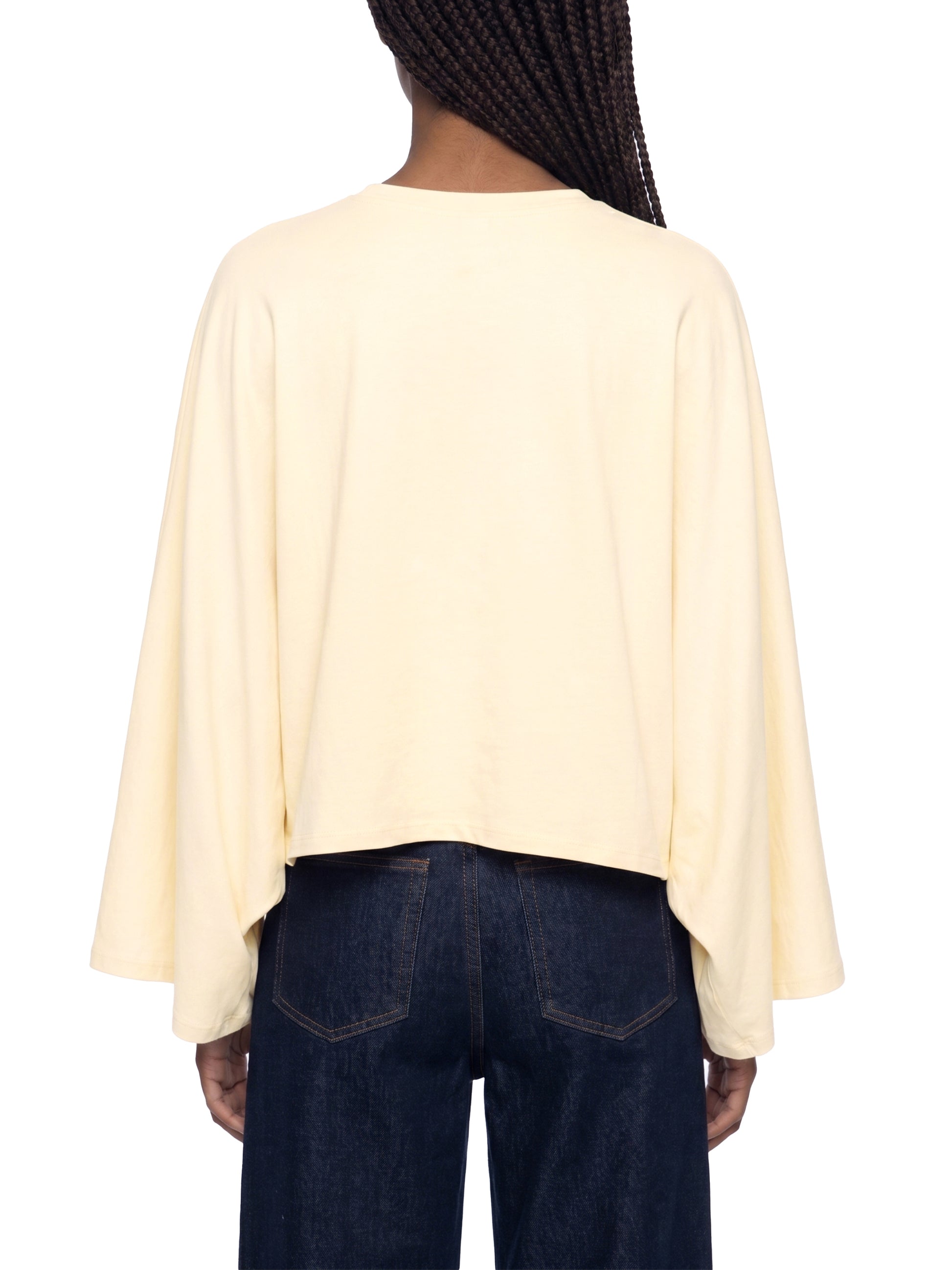 Person wearing a light yellow cape over dark blue jeans on a white background