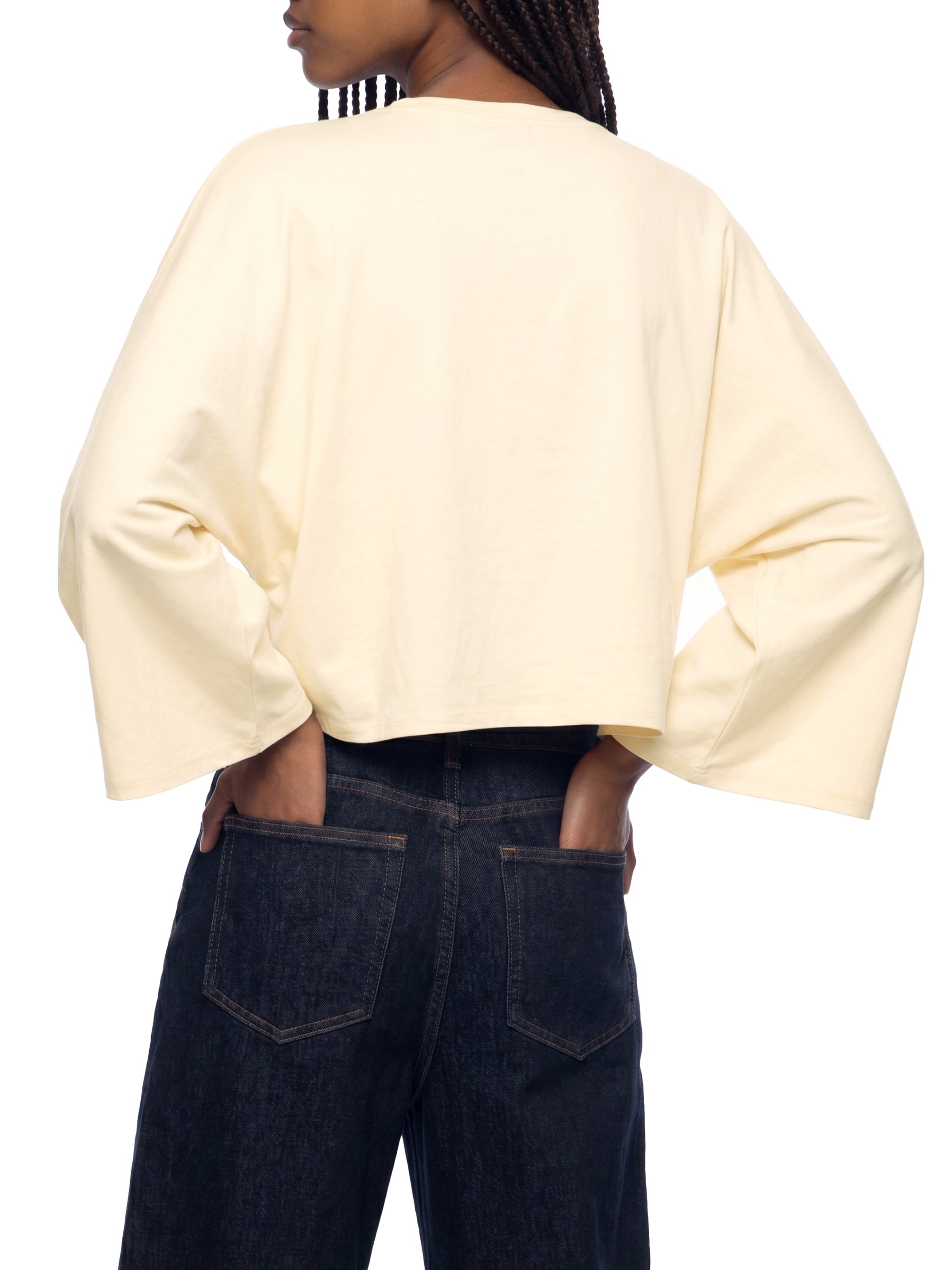 Person wearing a light yellow sweater and dark jeans on a white background